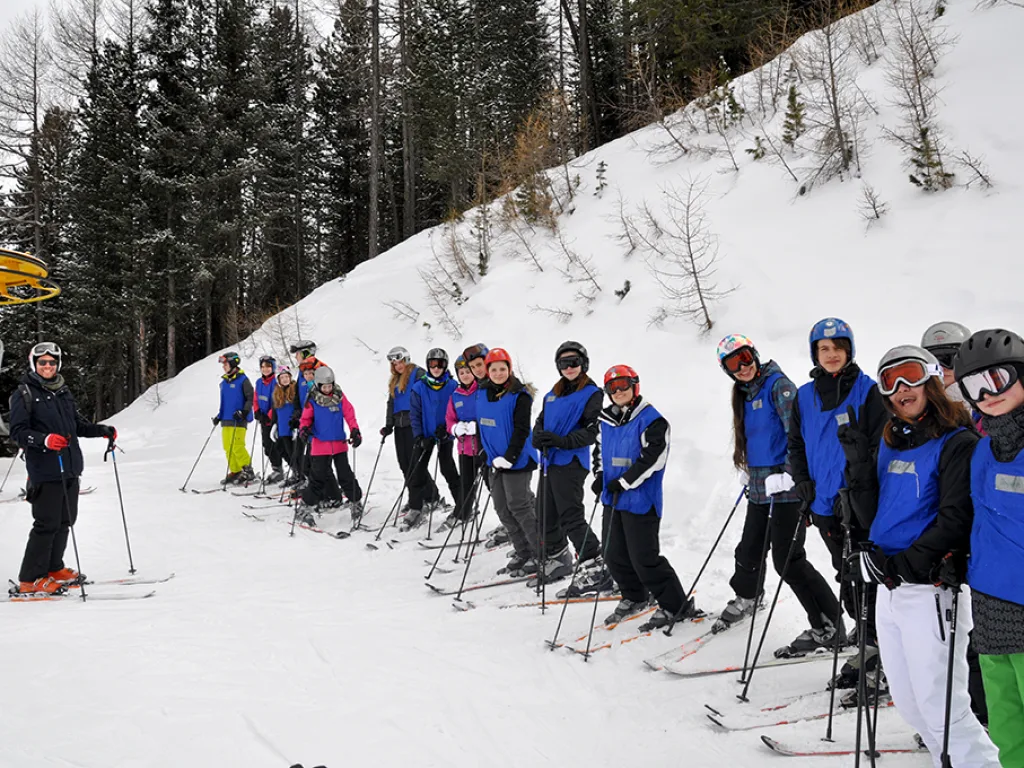 Skigruppe steht am Pistenrand vor dem Wald.